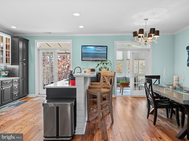 kitchen with an inviting chandelier, a kitchen breakfast bar, hanging light fixtures, ornamental molding, and light hardwood / wood-style floors