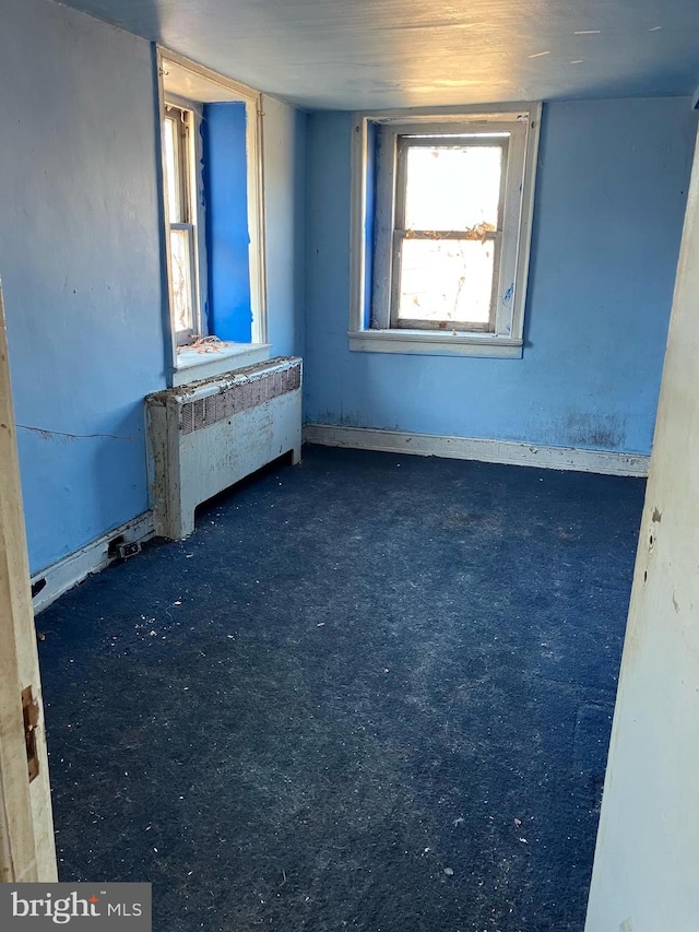 spare room featuring dark colored carpet and radiator heating unit