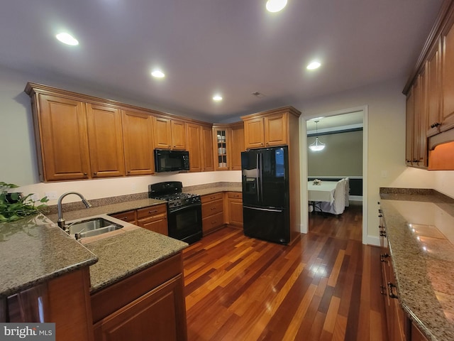 kitchen with stone counters, dark hardwood / wood-style flooring, black appliances, and sink