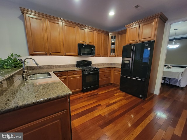 kitchen with dark wood-type flooring, black appliances, sink, hanging light fixtures, and light stone countertops