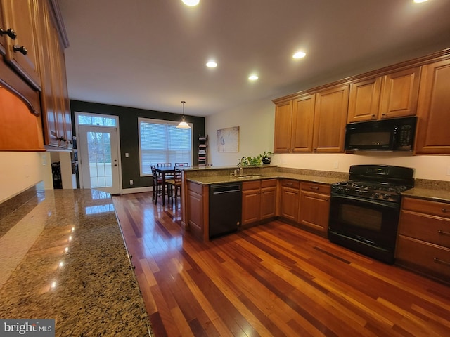 kitchen featuring kitchen peninsula, dark stone counters, black appliances, dark hardwood / wood-style floors, and hanging light fixtures