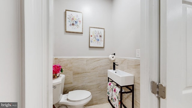 bathroom featuring toilet, tile walls, and sink