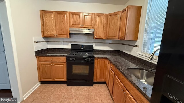 kitchen with light tile patterned floors, dark stone countertops, sink, and black gas range oven