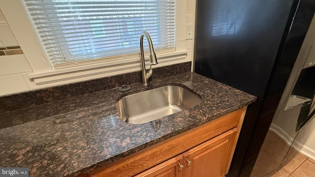 room details featuring black fridge, dark stone counters, sink, and light tile patterned flooring