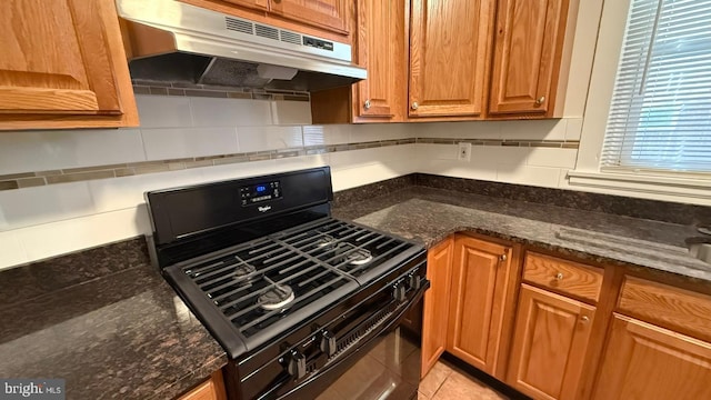 kitchen featuring black range with gas cooktop, decorative backsplash, dark stone counters, and light tile patterned floors