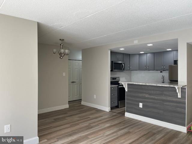 kitchen featuring appliances with stainless steel finishes, pendant lighting, an inviting chandelier, dark wood-type flooring, and kitchen peninsula