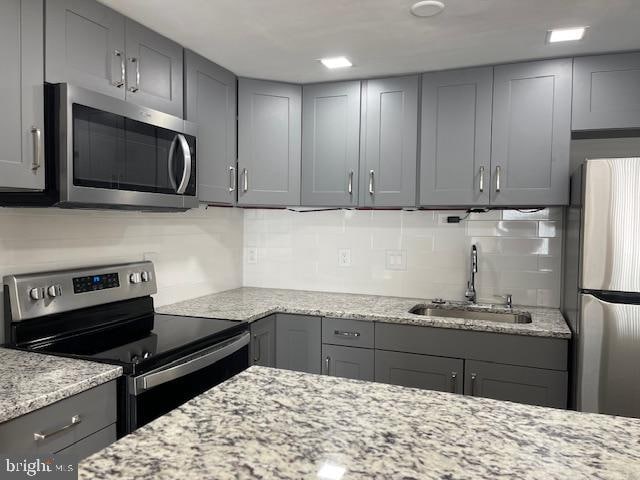 kitchen featuring sink, light stone counters, appliances with stainless steel finishes, backsplash, and gray cabinets