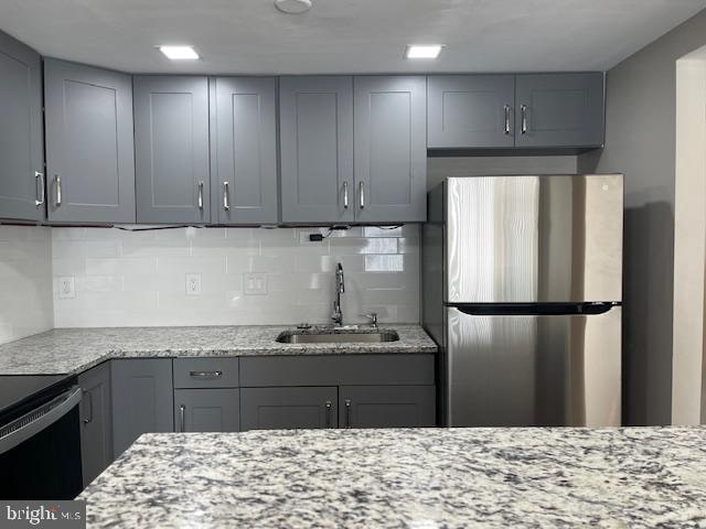 kitchen featuring gray cabinetry, stainless steel refrigerator, and light stone countertops