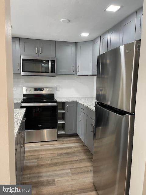 kitchen with stainless steel appliances, gray cabinets, and light stone countertops