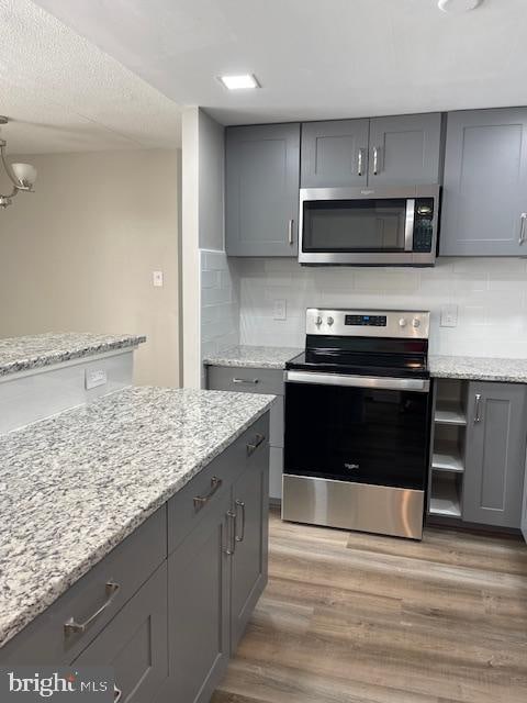 kitchen with hardwood / wood-style floors, appliances with stainless steel finishes, tasteful backsplash, and gray cabinetry