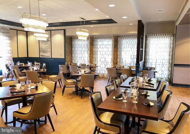 dining area with a raised ceiling, a chandelier, a wealth of natural light, and light hardwood / wood-style flooring