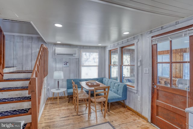 dining room featuring a wall mounted AC, wooden walls, and light hardwood / wood-style flooring