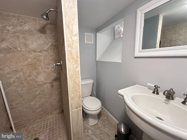 bathroom featuring tile patterned flooring, tiled shower, sink, and toilet