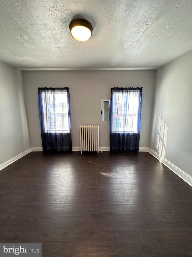 unfurnished room with a textured ceiling, radiator heating unit, a healthy amount of sunlight, and dark hardwood / wood-style floors