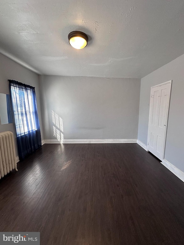 unfurnished room featuring a textured ceiling, radiator heating unit, and dark hardwood / wood-style flooring