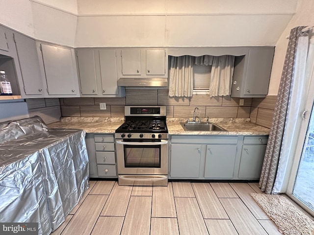 kitchen with decorative backsplash, sink, range hood, and stainless steel gas range