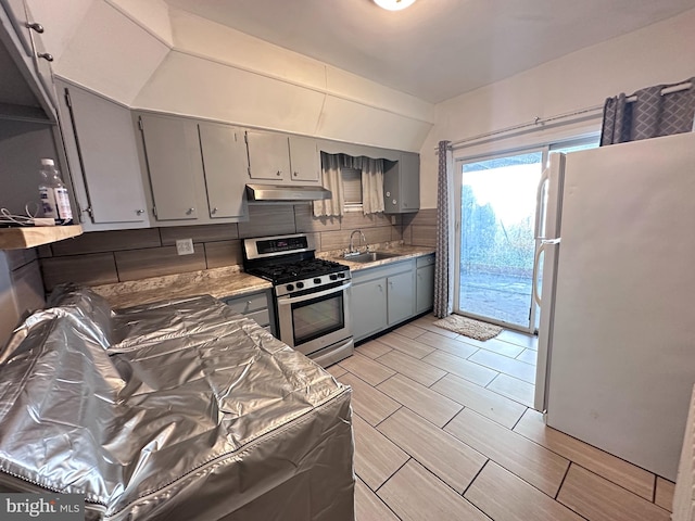 kitchen featuring stainless steel gas stove, white refrigerator, gray cabinets, sink, and decorative backsplash