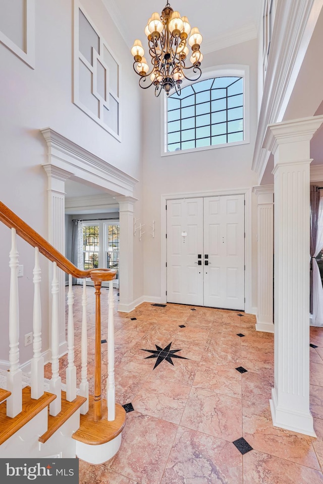 entryway with ornate columns, crown molding, a towering ceiling, and a chandelier