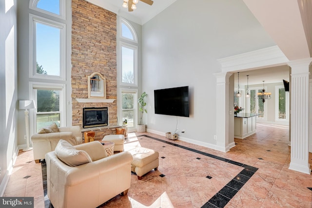 living room with ceiling fan with notable chandelier, decorative columns, high vaulted ceiling, and a stone fireplace