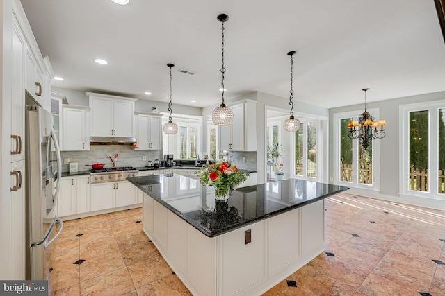 kitchen with a center island, stainless steel appliances, a notable chandelier, backsplash, and white cabinets