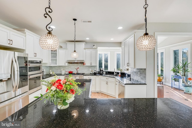 kitchen featuring dark stone countertops, white cabinets, hanging light fixtures, and appliances with stainless steel finishes