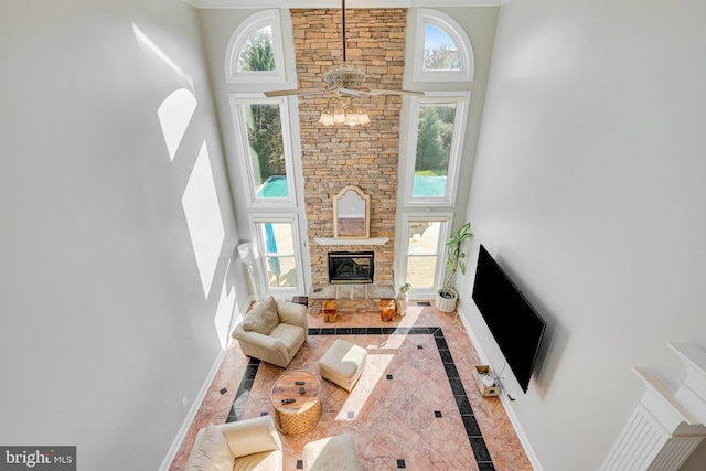 living room with a high ceiling, a stone fireplace, ceiling fan, and a healthy amount of sunlight