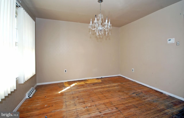 empty room with wood-type flooring and an inviting chandelier