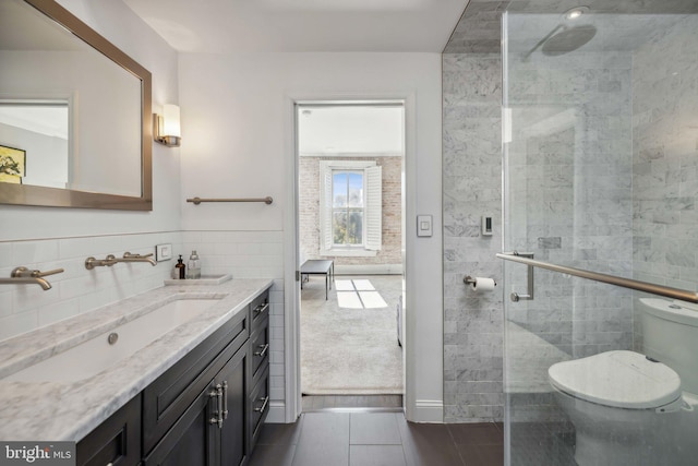 bathroom with vanity, a shower with door, tile patterned flooring, toilet, and tile walls