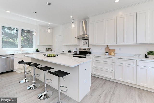 kitchen with white cabinetry, a center island, wall chimney range hood, pendant lighting, and appliances with stainless steel finishes