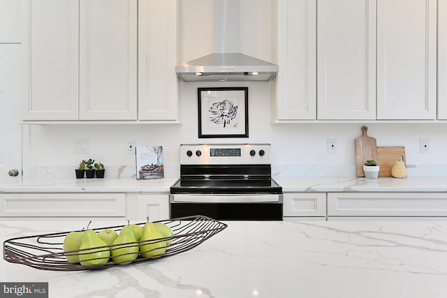 kitchen with light stone countertops, white cabinetry, stainless steel range with electric cooktop, and wall chimney range hood