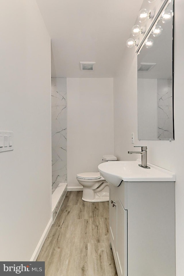 bathroom featuring a tile shower, vanity, wood-type flooring, and toilet