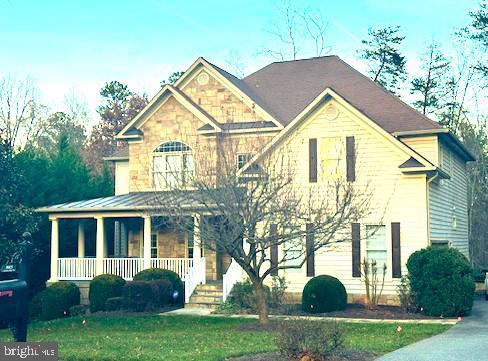 view of front facade featuring a front lawn, a standing seam roof, stone siding, a porch, and metal roof