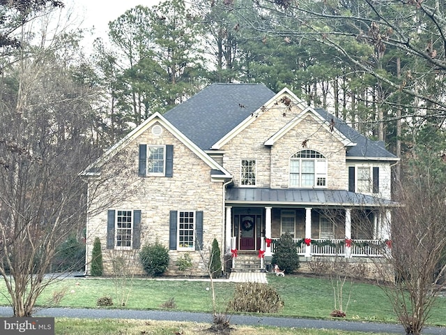 view of front of property with stone siding, covered porch, a front yard, and roof with shingles