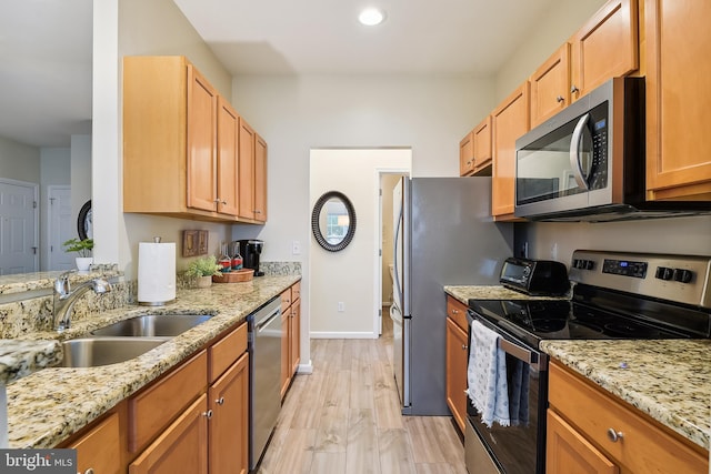 kitchen with light stone countertops, sink, stainless steel appliances, and light wood-type flooring