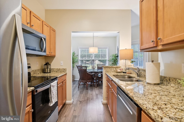 kitchen with light stone countertops, appliances with stainless steel finishes, sink, pendant lighting, and light hardwood / wood-style flooring