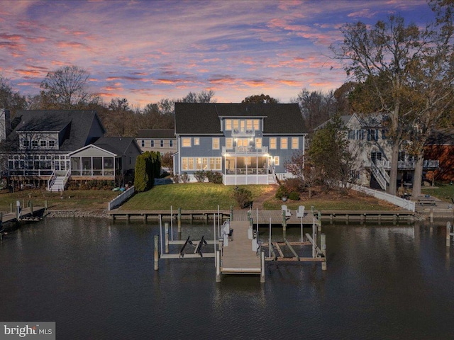 back house at dusk with a yard, a water view, and a balcony