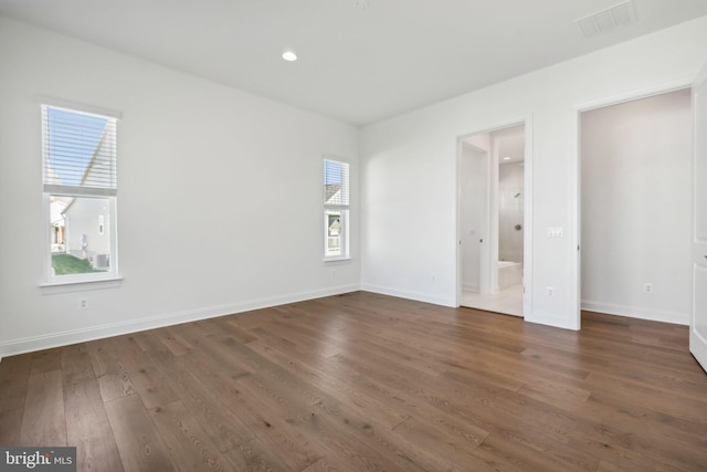 unfurnished bedroom with dark hardwood / wood-style floors, multiple windows, and connected bathroom