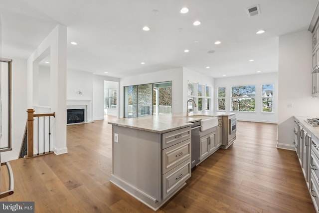 kitchen featuring sink, light stone countertops, an island with sink, gray cabinetry, and light wood-type flooring