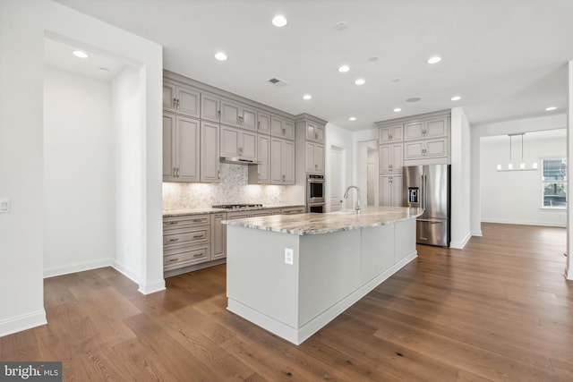 kitchen with stainless steel appliances, tasteful backsplash, an island with sink, and dark hardwood / wood-style flooring