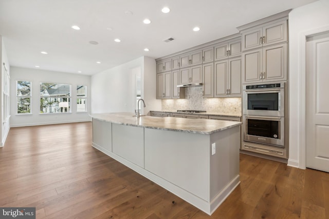 kitchen featuring backsplash, dark hardwood / wood-style floors, light stone counters, and appliances with stainless steel finishes