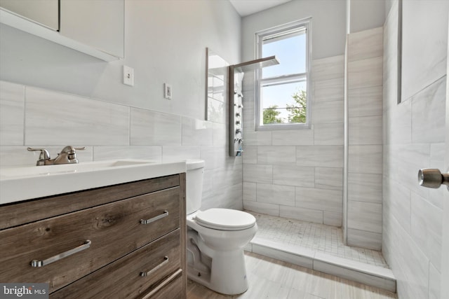 bathroom with vanity, toilet, a tile shower, and tile walls