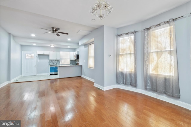 unfurnished living room with ceiling fan with notable chandelier and light wood-type flooring