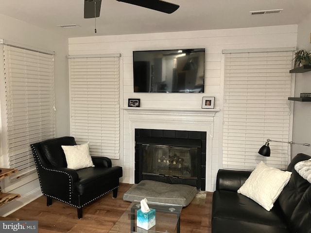 living room featuring hardwood / wood-style flooring, ceiling fan, and a tiled fireplace