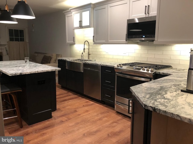 kitchen with white cabinets, hanging light fixtures, light hardwood / wood-style flooring, light stone counters, and stainless steel appliances