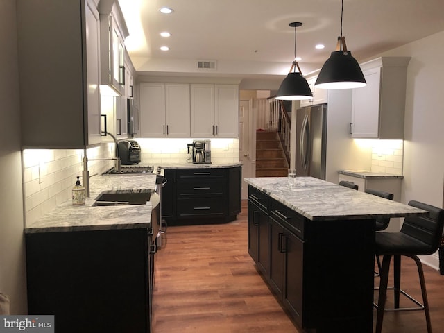 kitchen with decorative light fixtures, white cabinetry, stainless steel refrigerator, and a kitchen island