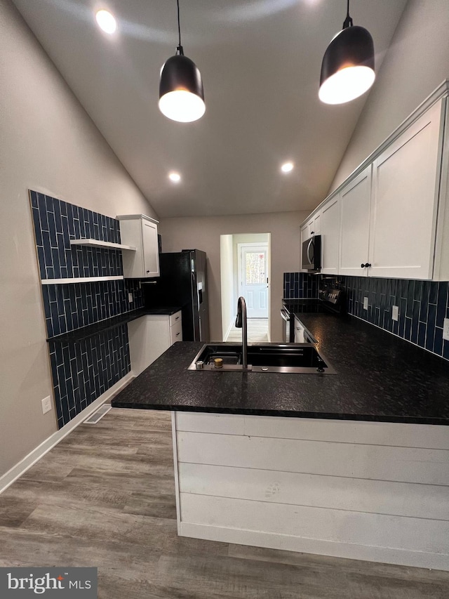 kitchen featuring hardwood / wood-style flooring, appliances with stainless steel finishes, kitchen peninsula, decorative light fixtures, and vaulted ceiling