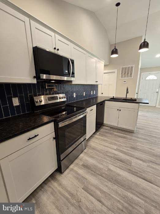 kitchen with stainless steel appliances, kitchen peninsula, sink, light wood-type flooring, and decorative light fixtures