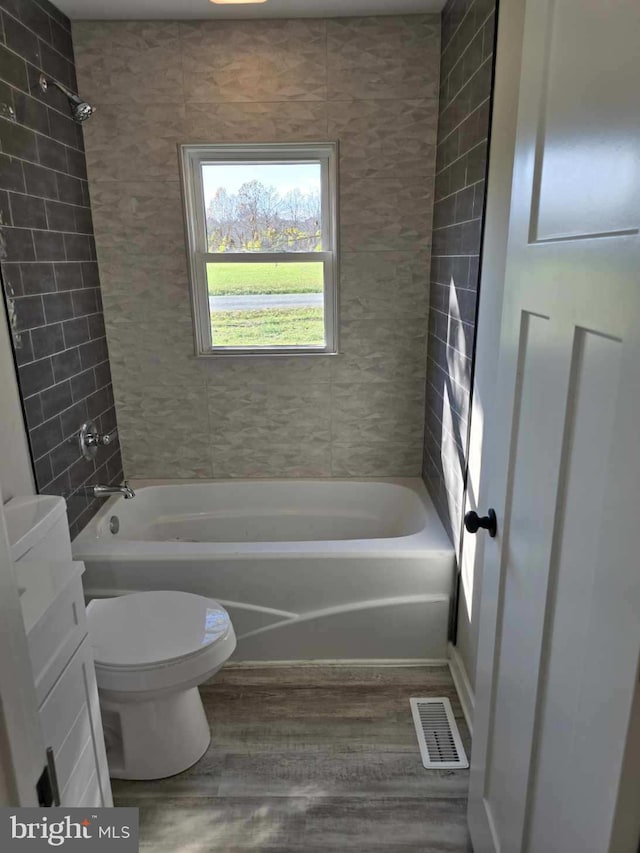 bathroom with toilet, tiled shower / bath combo, and hardwood / wood-style floors