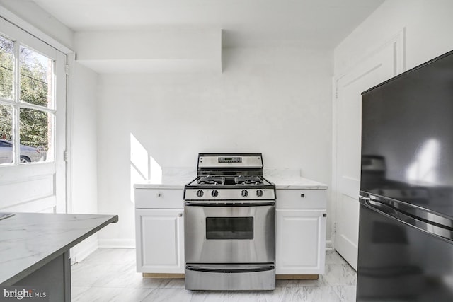 kitchen featuring black fridge, stainless steel range with gas stovetop, light stone counters, and white cabinets