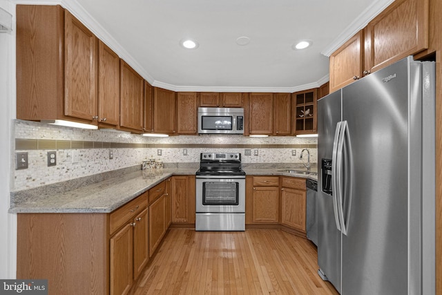 kitchen with light stone counters, light hardwood / wood-style flooring, sink, ornamental molding, and appliances with stainless steel finishes